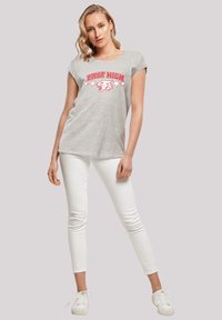 Grå bomulds t-shirt med en rød "EAST HIGH" grafik og ørnedesign, parret med hvide skinny jeans og hvide sneakers.