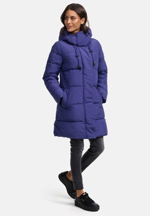 Purple padded coat with hood, featuring a zip closure, adjustable drawstrings, and two side pockets. Worn over dark jeans and black sneakers.