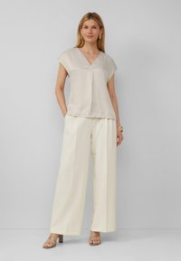 Lichtbeige, kortärmad top met een V-hals en een vloeiende ontwerp, gecombineerd met wijd uitlopende witte broek en neutrale blokhak sandalen.