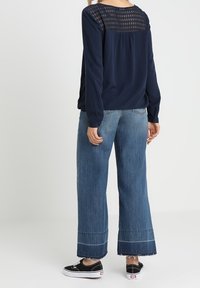 Marineblaues Langarmoberteil mit strukturiertem Rücken, kombiniert mit weitem Denim-Jeans mit ausgefransten Säumen und hellem Waschung. Schwarze Sneaker runden den Look ab.