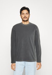 Camisa de manga larga con cuello redondo en gris oscuro. Tejido suave con una textura lisa y un sutil detalle de costura. Combinada con jeans de mezclilla azul claro.