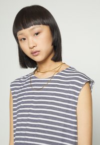 Top sem mangas às riscas azul marinho e brancas com um corte descontraído, exibindo uma textura suave. Apresenta colares de corrente dourada como detalhes.