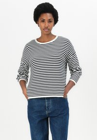 Sweater de mangas longas em preto e branco às riscas com decote redondo, textura suave e corte descontraído, combinado com jeans azuis.