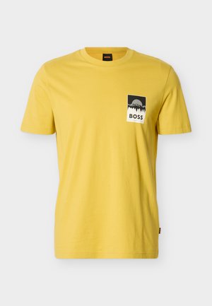 Camiseta amarilla de manga corta con cuello redondo, con un gráfico rectangular en blanco y negro de montañas y árboles sobre la palabra "BOSS" en el pecho.