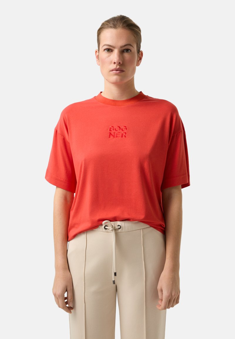 Rood katoenen T-shirt met een ronde hals en korte mouwen, voorzien van een geborduurd "BOGNER"-logo in het midden. Gecombineerd met beige broek.