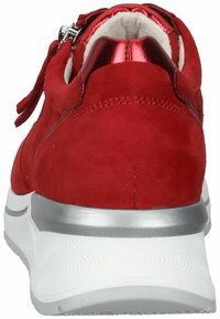 Zapatilla de ante rojo con un acento metálico rojo en el talón, suela blanca texturizada y un detalle de cierre con cremallera en la parte trasera para un acceso fácil.
