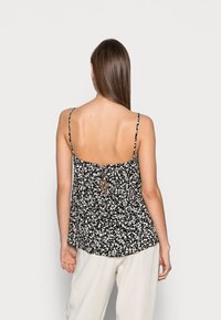 Top fluido floreale in bianco e nero con spalline regolabili, dettaglio con fiocco sul retro e vestibilità ampia. Tessuto morbido con un motivo testurizzato.