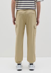 Pantalones cargo beige con una cintura elástica y puños fruncidos. Cuenta con dos bolsillos laterales y dos traseros. Se llevan con zapatillas deportivas.