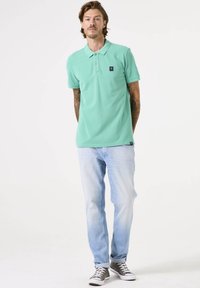 Camisa de polo verde menta con cuello, mangas cortas y un pequeño parche con logo. Combinada con jeans de color azul claro y zapatillas grises.