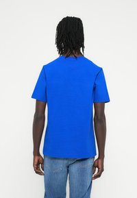 Μπλε βαμβακερό μπλουζάκι με κοντά μανίκια, στρογγυλή λαιμόκοψη, άνετη εφαρμογή και απαλό υφή. Φοριέται με ανοιχτό μπλε τζιν παντελόνι.