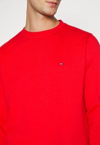 Rode sweatshirt met een ronde hals en een gladde textuur. Bevat een klein merklogo op de linkerborst. Eenvoudig ontwerp zonder patronen.