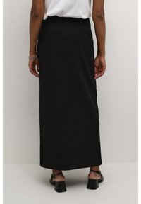 Jupe noire longue, avec une texture lisse, dotée d'une taille ajustée et d'une silhouette droite. Portée avec des sandales à talons et à lanières.