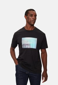 Camiseta de algodón negra con un estampado gráfico multicolor y el texto "Calvin Klein Jeans" en el centro; diseño de mangas cortas y cuello redondo.