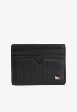 Tarjetero de cuero negro con parte frontal perforada, tres ranuras para tarjetas y un pequeño logo rectangular en rojo, blanco y azul en la parte inferior derecha.
