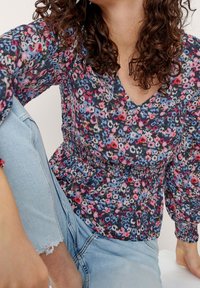 Blusa a fantasia floreale in blu scuro, con fiori rosa, rossi e bianchi, scollatura a V, maniche lunghe e dettaglio di vita arricciata.