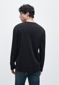 Svart långärmad tröja med rund halsringning, avslappnad passform och mjuk textur. Matchad med blå jeans, sedd bakifrån.