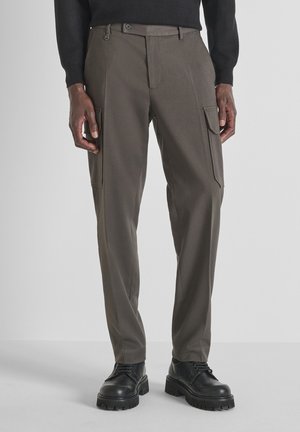 Pantalons cargo ajustés en tissu vert olive foncé avec deux poches latérales, passants de ceinture et fermeture éclair à l'avant. Fini texturé. Associés à des chaussures noires.