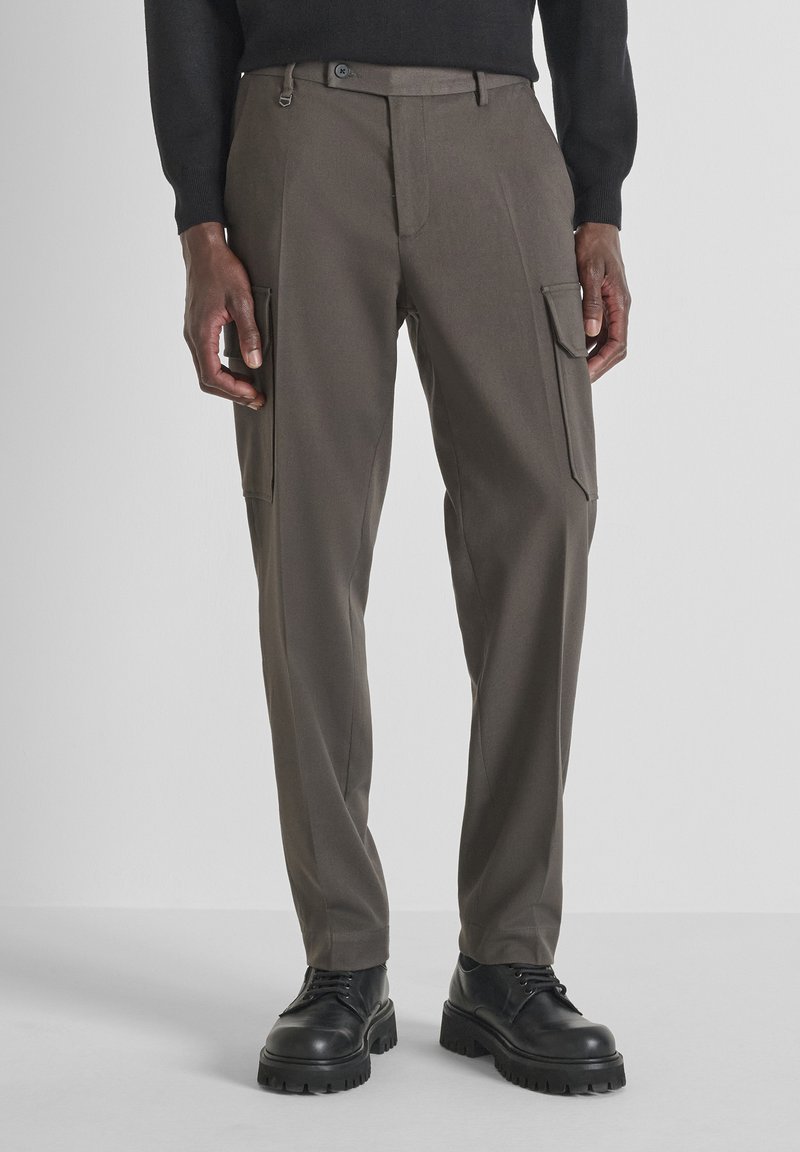 Pantaloni cargo slim-fit in tessuto verde oliva scuro con due tasche laterali, passanti per cintura e chiusura con zip frontale. Finitura testurizzata. Abbinati a scarpe nere.