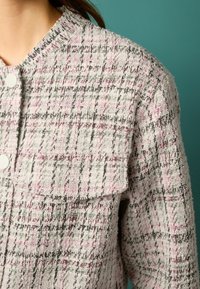 Giacca testurizzata in rosa chiaro, nero e crema con un motivo a quadri, dotata di scollatura rotonda e chiusura con un singolo bottone.