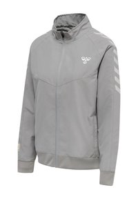 Jasnoszara kurtka na zamek z wysokim kołnierzem, logo na lewej piersi oraz odblaskowymi pasami w kształcie jodełki na prawym rękawie.