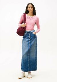 Gonna lunga di jeans con motivo floreale, abbinata a un maglione rosa a maniche lunghe e sneakers bianche. Una borsa a tracolla bordeaux completa l'outfit.