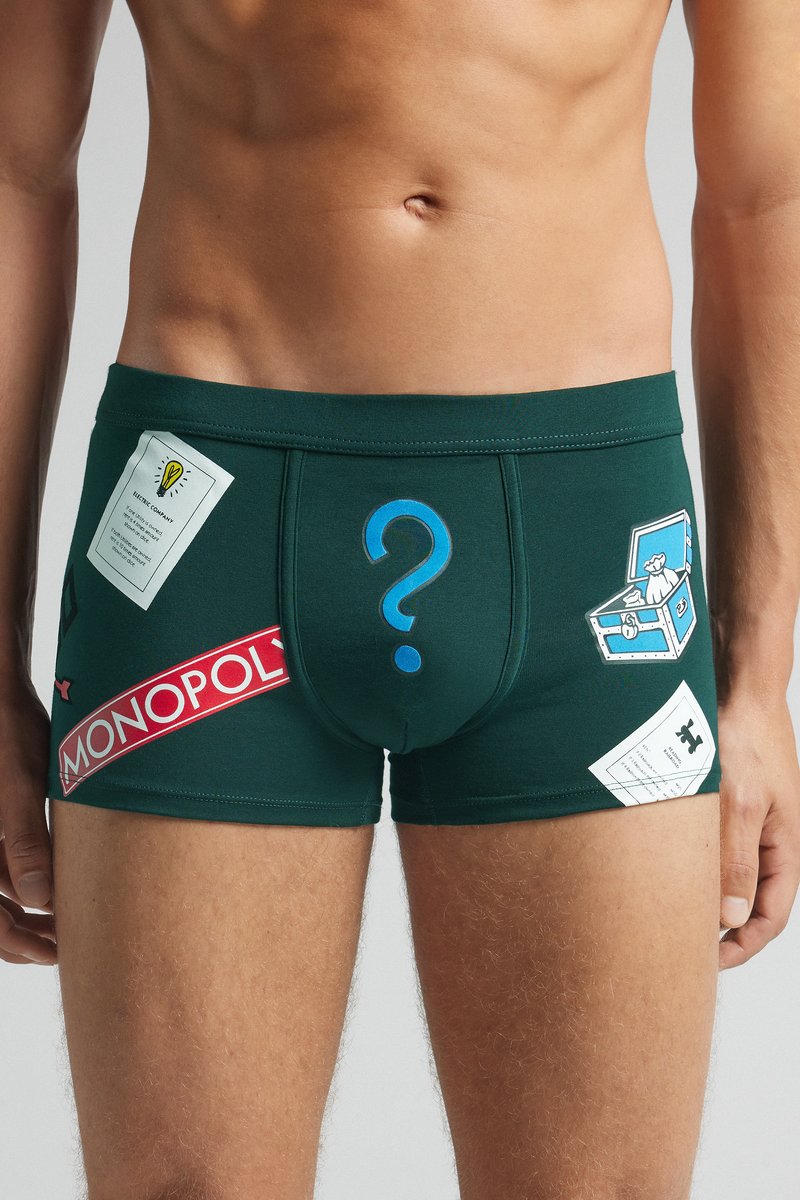 Boxer shorts verdes con acentos impresos de Monopoly, que incluyen un signo de interrogación, piezas del juego y etiquetas en colores vibrantes.