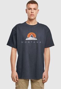 Donkergrijze katoenen t-shirt met een bergafbeelding en een oranje zon. "MONTANA" tekst onder het ontwerp, relaxte pasvorm met korte mouwen.