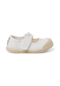 Zapato Mary Jane de lona blanca con una correa de velcro, suela de goma beige y punta redondeada. Presenta una pequeña etiqueta colorida en el lateral.