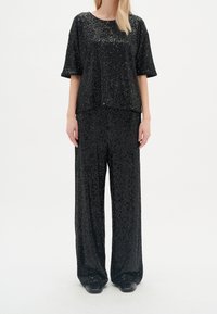 Svart paljett-topp med korta ärmar och matchande löst sittande paljettbyxor. Slät textur, glänsande yta och avslappnad silhuett.