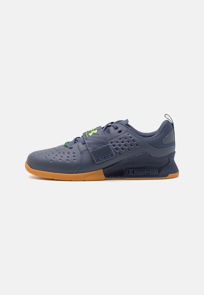 Athletic shoes in navy and gray synthetic material with perforations, rubber sole, green accents, and adjustable Velcro strap.