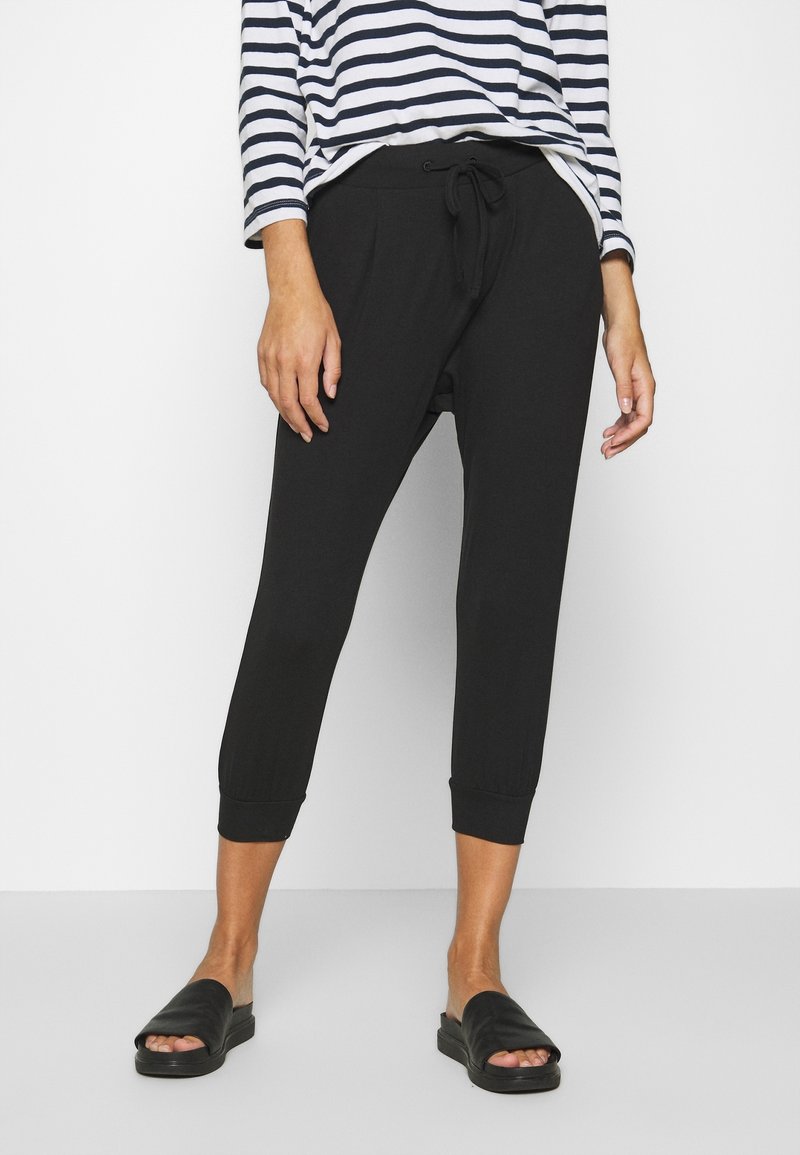 Pantalons noirs courts avec taille à cordon et poignets élastiques, associés à un haut à manches longues rayé et des sandales noires à glissière.