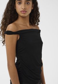 Juodas off-shoulder viršus, pagamintas iš minkštos medžiagos, su susiraukšlėjusiomis šoninėmis detalėmis ir prigludusia siluetu. Lygi tekstūra be raštų.