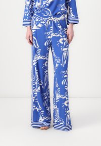 Blauwe patroon wijde broek heeft een bloemenontwerp in het wit, met een tailleband met trekkoord en gestreepte accenten aan de zoom en manchetten.