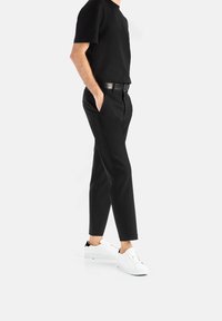 Černé bavlněné tričko, černé kalhoty slim fit s kapsami, doplněné o bílé tenisky s černými akcenty.