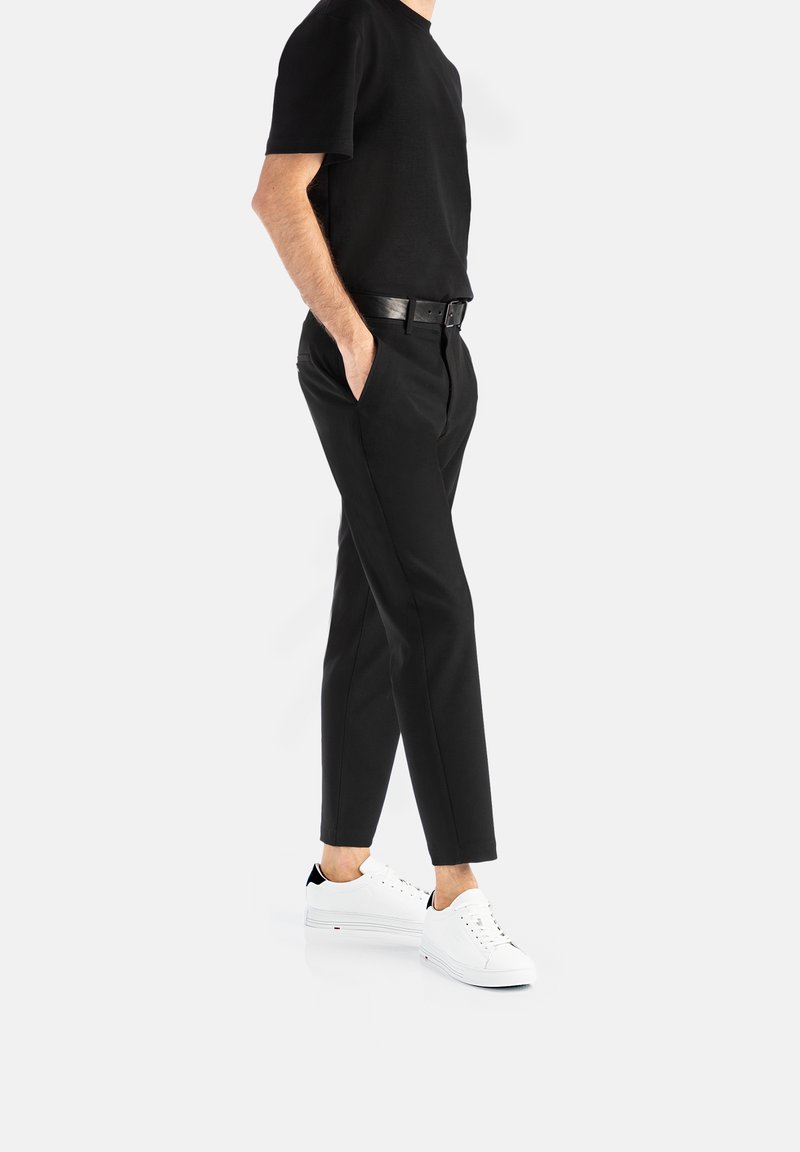 Černé bavlněné tričko, černé kalhoty slim fit s kapsami, doplněné o bílé tenisky s černými akcenty.