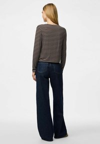 Brun och vit randig långärmad topp i kombination med högmidjade mörk denimjeans. Har en åtsittande passform och mjuk tygstruktur.