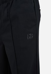 Pantalons noirs en tissu texturé avec une taille élastique et un logo PGDR discrètement brodé sur la poche.