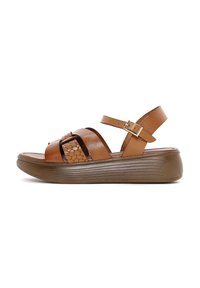 Sandalias de cuero marrón con correas ajustables en el tobillo, detalle trenzado en la parte superior y una suela de plataforma texturizada.