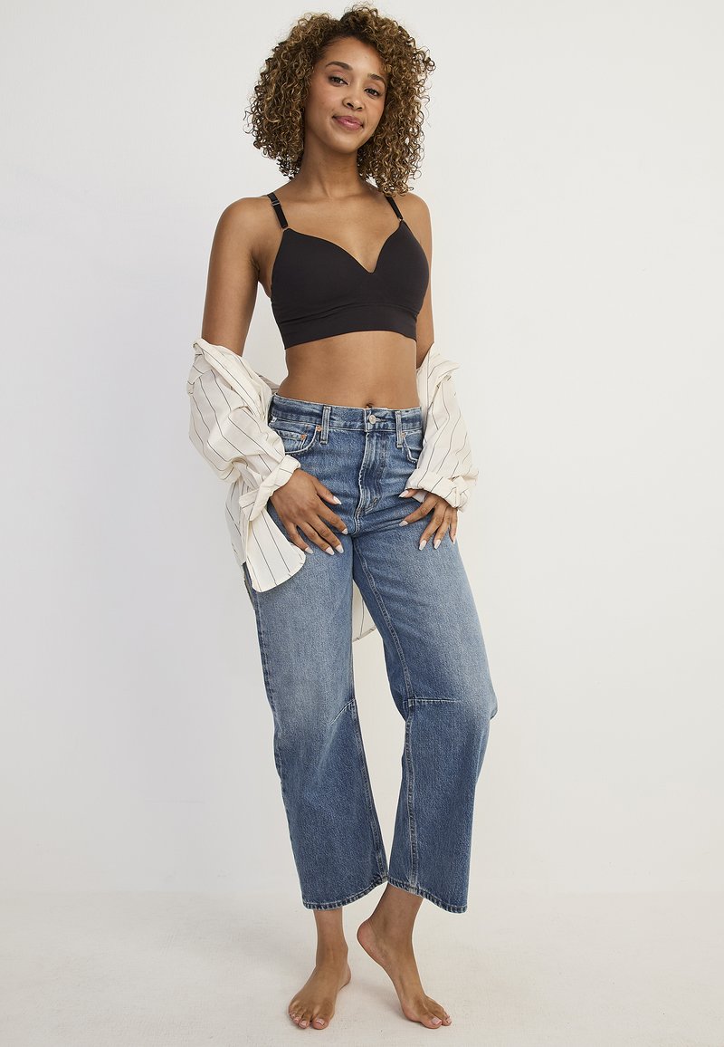 Svart bralette, blå högmidjade jeans och en lös vit randig skjorta. Har en cropped design, mjuk textur och avslappnad passform.