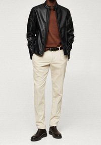 Giacca di pelle nera con zip, maglione marrone, pantaloni color crema e stivali alla caviglia marrone scuro. Outfit casual con un design aderente.