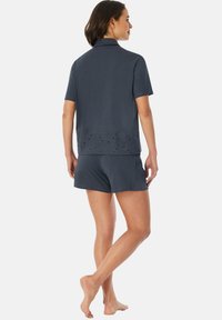 Navyblå loungewear-set bestående av en kortärmad topp med krage och detaljer i ögla, tillsammans med matchande shorts. Mjuk tygkvalitet.