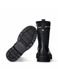 Ein Paar schwarze Knöchelstiefel mit groben Profilsohlen, Reißverschluss und einem gerippten Strickbund mit weißen Streifen.