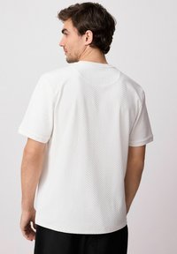 White short-sleeve t-shirt made from textured fabric, featuring a rounded neckline and a relaxed fit, with subtle seams along the back.