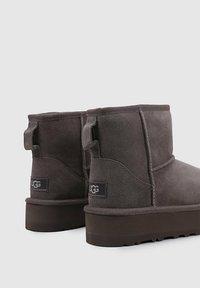 Botas de tobillo de ante gris con una textura suave, que cuentan con una suela plana, tiradores en el talón y una etiqueta de la marca en el lateral.