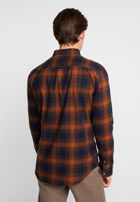 Camisa de franela para hombre en cuadros azul marino y naranja. Presenta mangas largas, puños abotonados y un dobladillo redondeado. Tejido suave con una textura lisa.