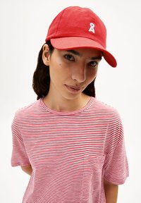 Rode honkbalpet met een wit lintlogo, gedragen met een rood-wit gestreepte t-shirt. Eenvoudig ontwerp, katoenen materiaal, casual pasvorm.