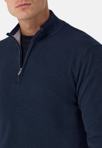 Laivastonsininen poolopaita puolivälillä vetoketjua oleva kaulus, valmistettu pehmeästä neulemateriaalista, jossa on sileä rakenne ja hienovaraiset ompelut.