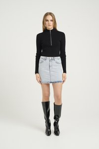 Dolcevita nero a costine con zip argentata, abbinato a una mini-gonna in denim chiaro e stivali neri lucidi al ginocchio, su uno sfondo neutro.