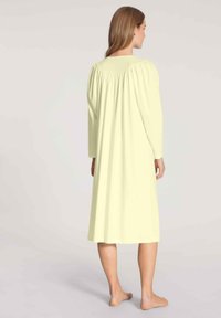 Camicia da notte lunga, di un leggero colore giallo chiaro, con tessuto arricciato sulle spalle e maniche lunghe, che arriva sotto il ginocchio, realizzata in materiale morbido.