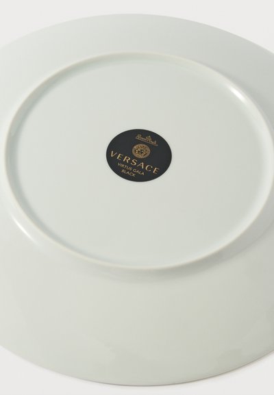 Λευκό πορσελάνινο πιάτο με μαύρη και χρυσή ετικέτα Versace Virtus Gala Black στο κέντρο κάτω μέρος.